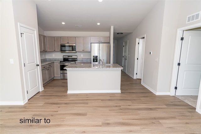 kitchen with appliances with stainless steel finishes, light stone counters, light hardwood / wood-style flooring, and an island with sink