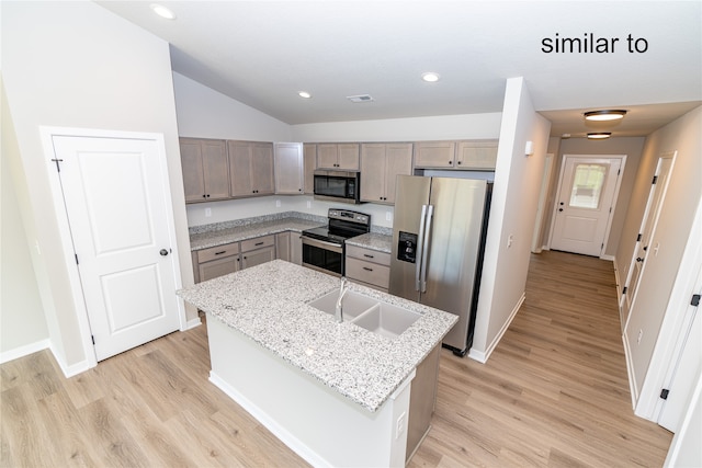 kitchen with lofted ceiling, light hardwood / wood-style flooring, a center island with sink, appliances with stainless steel finishes, and light stone counters