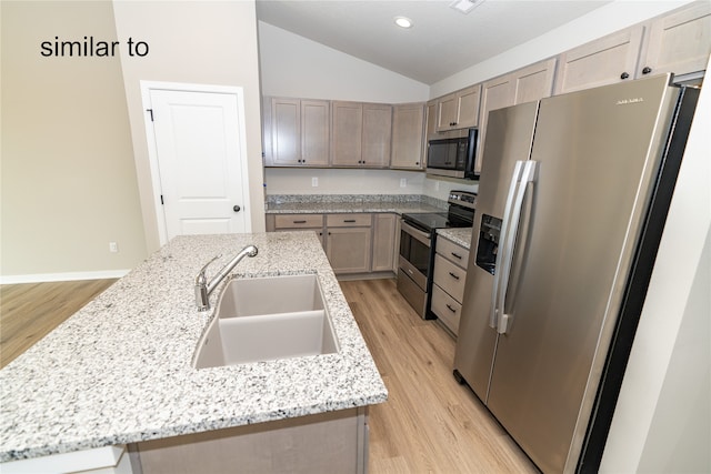 kitchen with an island with sink, sink, vaulted ceiling, appliances with stainless steel finishes, and light hardwood / wood-style floors