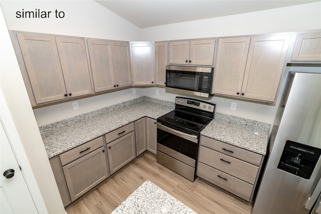 kitchen featuring stainless steel appliances, vaulted ceiling, light brown cabinetry, light stone counters, and light hardwood / wood-style floors