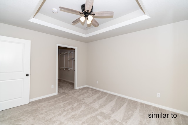 unfurnished bedroom with a closet, ceiling fan, a raised ceiling, and a walk in closet