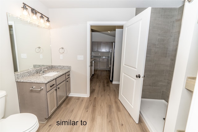 bathroom featuring vanity, tiled shower, wood-type flooring, and toilet