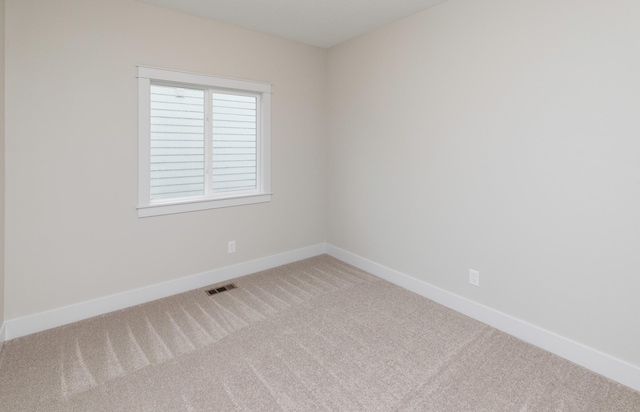 spare room featuring baseboards, visible vents, and light carpet