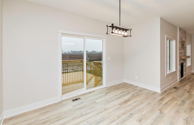 unfurnished dining area featuring a stone fireplace, visible vents, wood finished floors, and baseboards