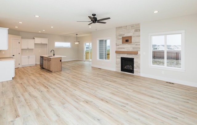 unfurnished living room featuring baseboards, recessed lighting, a sink, a stone fireplace, and light wood-type flooring