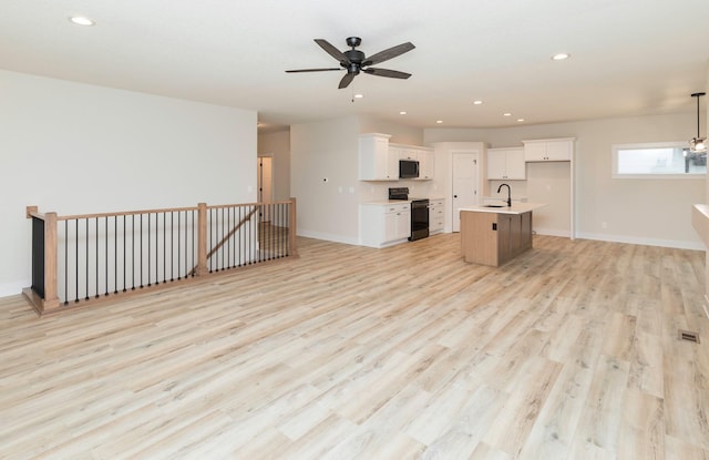 kitchen featuring open floor plan, black electric range oven, light wood-type flooring, and a sink