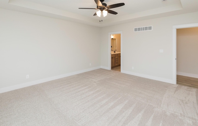 empty room featuring visible vents, light carpet, baseboards, a raised ceiling, and ceiling fan