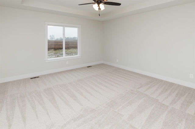 carpeted spare room featuring a tray ceiling, baseboards, and visible vents