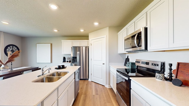 kitchen with sink, light wood-type flooring, stainless steel appliances, a textured ceiling, and white cabinets