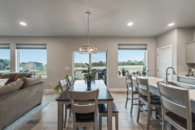 dining area with light hardwood / wood-style flooring, a healthy amount of sunlight, sink, and an inviting chandelier