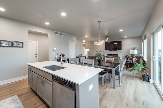 kitchen featuring sink, light wood-type flooring, dishwasher, and an island with sink