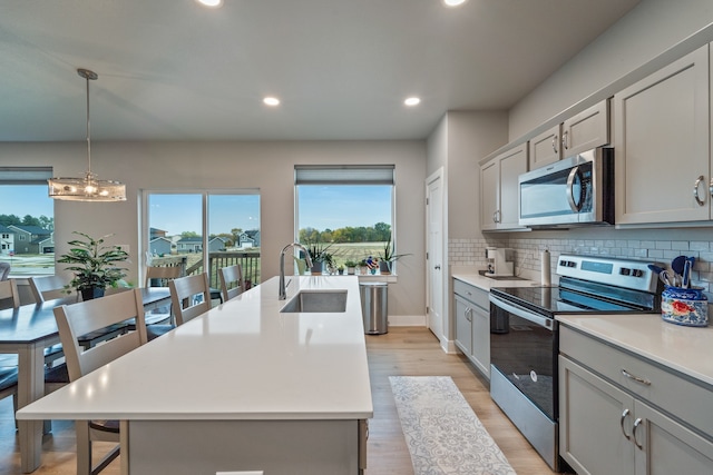 kitchen featuring appliances with stainless steel finishes, sink, an island with sink, and gray cabinets