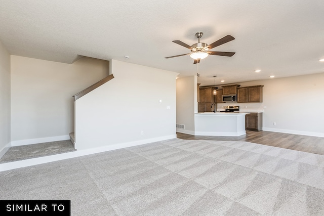 unfurnished living room featuring ceiling fan, a textured ceiling, and light colored carpet