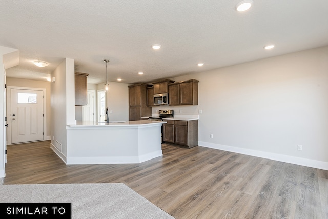 kitchen featuring a textured ceiling, appliances with stainless steel finishes, light hardwood / wood-style flooring, and decorative light fixtures