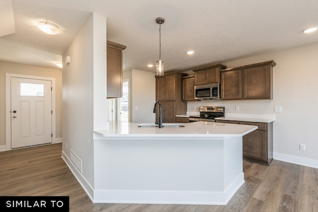 kitchen featuring a textured ceiling, light hardwood / wood-style flooring, sink, pendant lighting, and stainless steel appliances