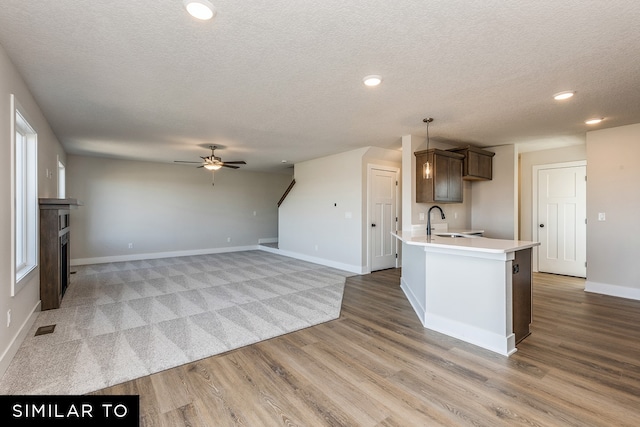 kitchen with sink, a textured ceiling, dark brown cabinets, light hardwood / wood-style floors, and ceiling fan