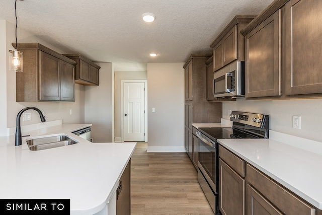 kitchen featuring a textured ceiling, light wood-type flooring, stainless steel appliances, sink, and decorative light fixtures