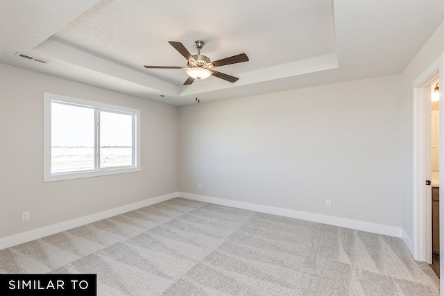 carpeted spare room with ceiling fan and a raised ceiling