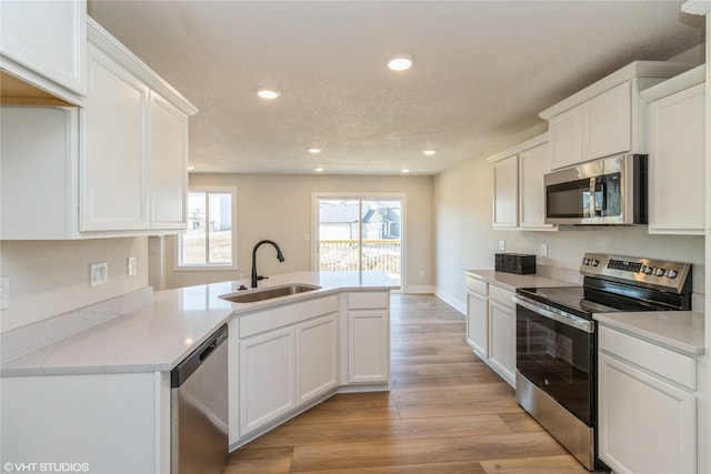 kitchen with recessed lighting, appliances with stainless steel finishes, light wood-style flooring, a peninsula, and a sink