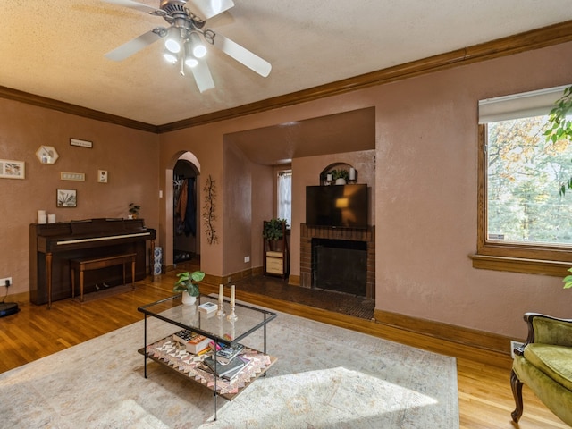 living room featuring crown molding, a brick fireplace, wood-type flooring, and ceiling fan