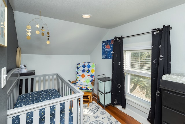 bedroom featuring lofted ceiling, hardwood / wood-style floors, and a nursery area