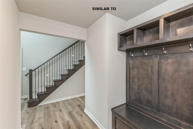 mudroom featuring light wood-style flooring, baseboards, and a textured ceiling