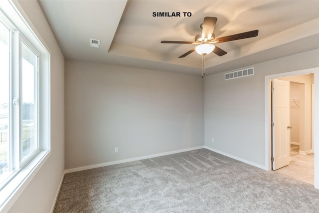 empty room featuring light carpet, a raised ceiling, visible vents, and baseboards