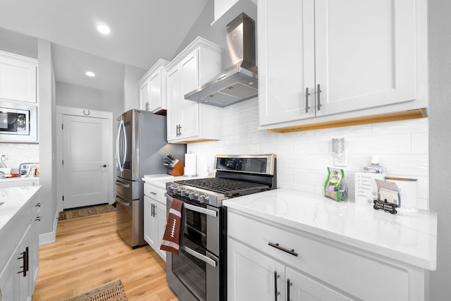 kitchen with light stone countertops, white cabinetry, light hardwood / wood-style floors, stainless steel appliances, and wall chimney exhaust hood