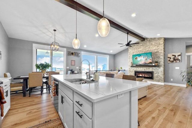 kitchen with sink, a fireplace, lofted ceiling with beams, light hardwood / wood-style floors, and a center island with sink