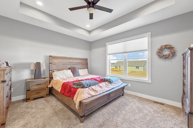 bedroom with a raised ceiling, light carpet, and ceiling fan