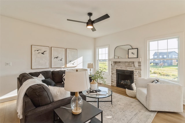 living room with ceiling fan, a stone fireplace, and light hardwood / wood-style flooring