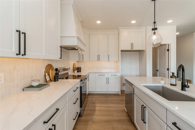 kitchen featuring appliances with stainless steel finishes, sink, light wood-type flooring, white cabinetry, and premium range hood