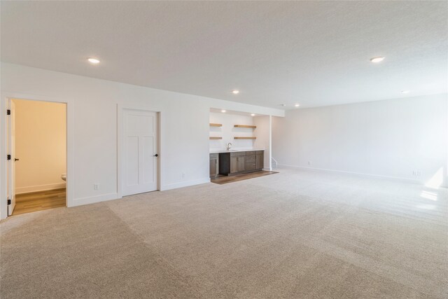 unfurnished living room with sink, light colored carpet, and a textured ceiling