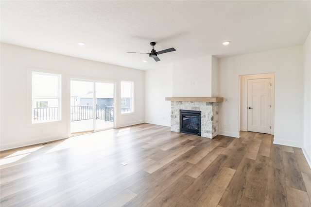 unfurnished living room with a stone fireplace, a textured ceiling, light hardwood / wood-style floors, and ceiling fan