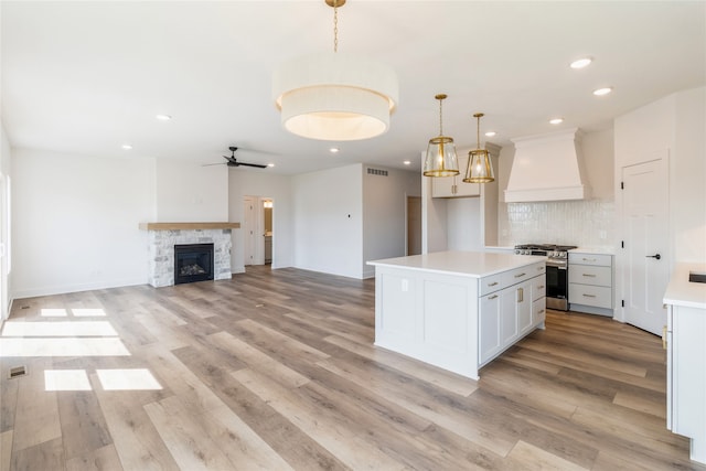 kitchen with stainless steel gas stove, hanging light fixtures, white cabinets, light wood-type flooring, and premium range hood