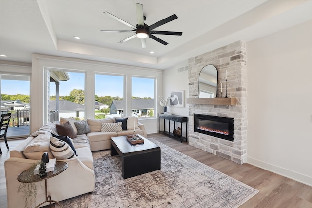 living room with hardwood / wood-style floors, a raised ceiling, a fireplace, and ceiling fan