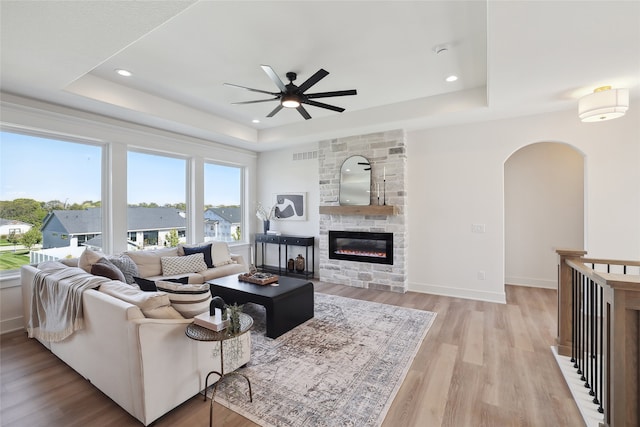 living room with a fireplace, a tray ceiling, light wood-type flooring, and ceiling fan