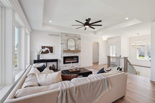 living room with a tray ceiling, light hardwood / wood-style flooring, and a stone fireplace