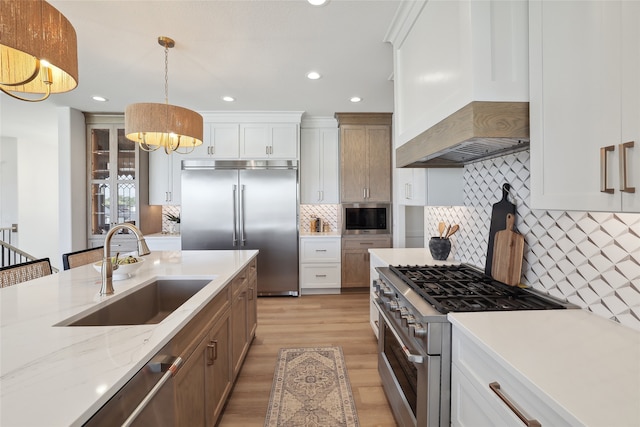 kitchen featuring built in appliances, hanging light fixtures, custom exhaust hood, and white cabinets