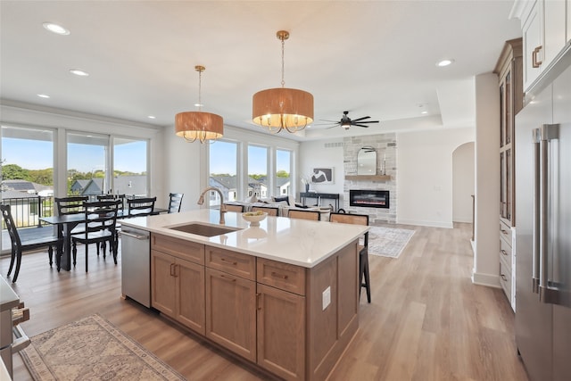 kitchen featuring sink, a large fireplace, stainless steel appliances, pendant lighting, and a kitchen island with sink