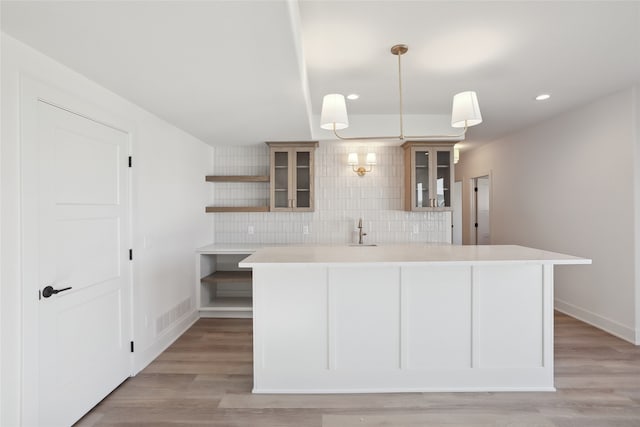 kitchen with backsplash, sink, hanging light fixtures, and light wood-type flooring