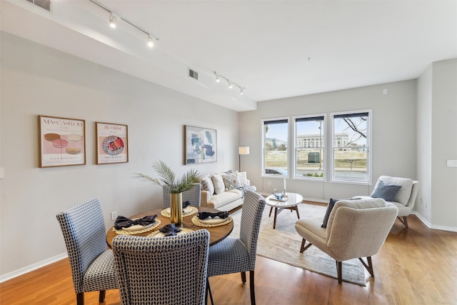 dining area with light wood-type flooring, visible vents, and baseboards