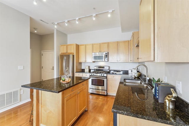 kitchen featuring sink, a center island, dark stone countertops, stainless steel appliances, and light hardwood / wood-style floors