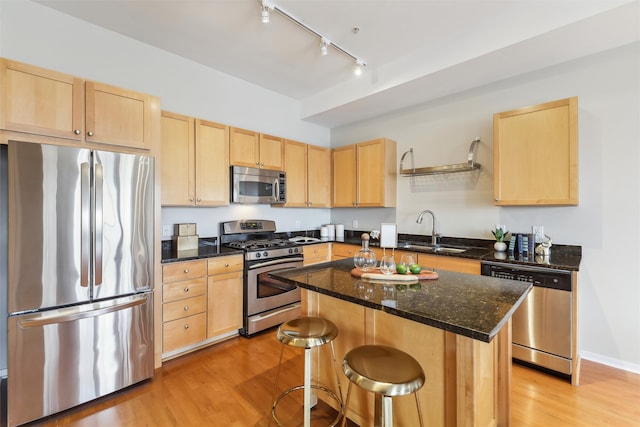 kitchen with sink, stainless steel appliances, a kitchen island, dark stone counters, and light brown cabinets