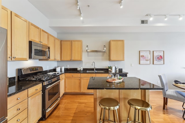 kitchen with sink, appliances with stainless steel finishes, light brown cabinets, dark stone counters, and light wood-type flooring