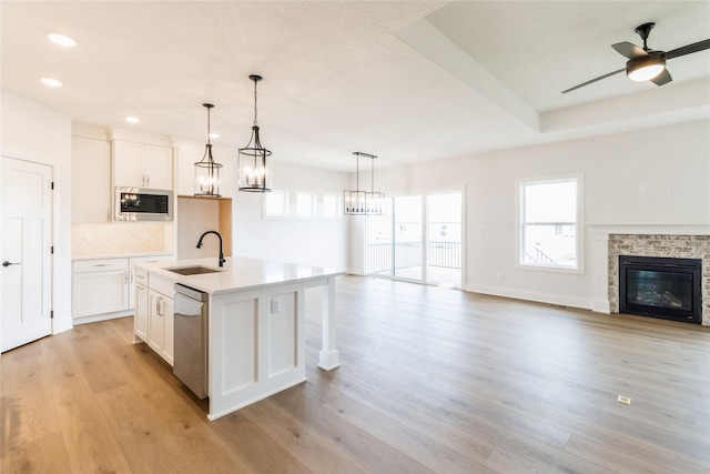 kitchen featuring sink, light wood-type flooring, stainless steel appliances, white cabinets, and a center island with sink