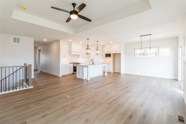 unfurnished living room with light hardwood / wood-style flooring, a tray ceiling, and ceiling fan with notable chandelier