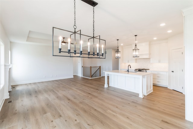 kitchen featuring white cabinetry, decorative light fixtures, a center island with sink, and light wood-type flooring