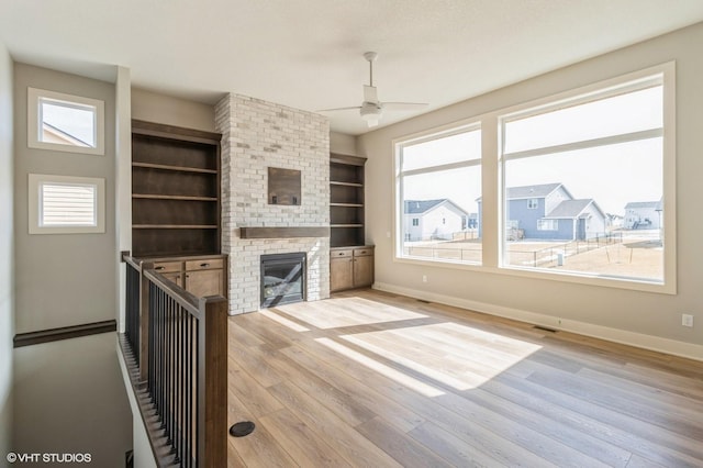 unfurnished living room featuring plenty of natural light, visible vents, a fireplace, and wood finished floors