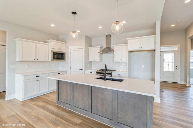 kitchen with wall chimney range hood, stainless steel microwave, and white cabinetry